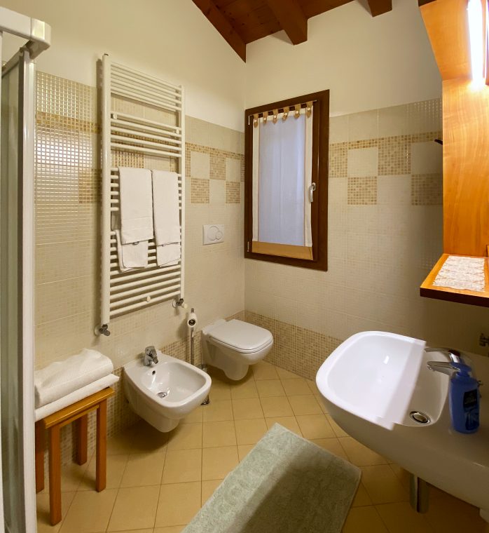 Il bagno privato di una camera, con la doccia, la finestra e il soffitto a travi