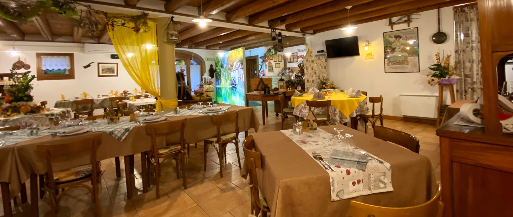 La sala del ristorante con i tavoli apparecchiati, le travi in legno e le tende gialle